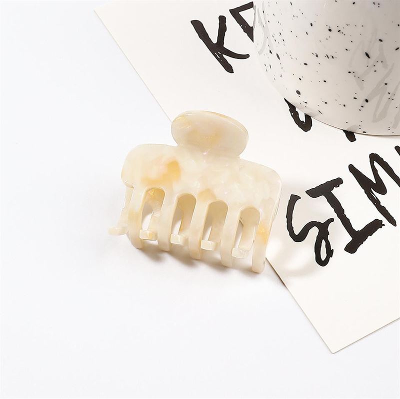 Anna Hårklemme - Cotton af Chris Rubin har et beige marmormønster og vises på hvidt papir med sort tekst ved siden af en stilfuld hvid kop med sorte prikker.