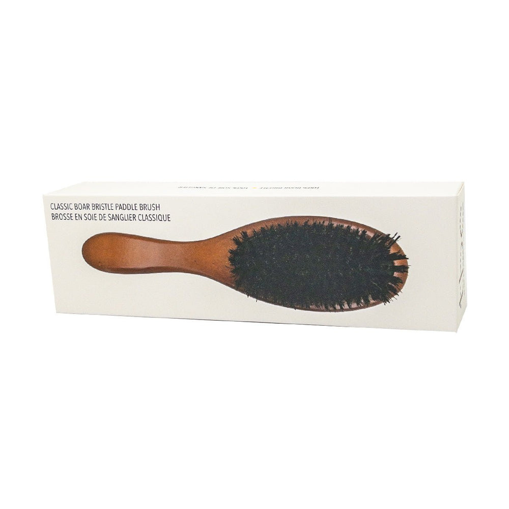 En rektangulær æske viser TBC's Classic Hårbørste med Boar Bristle paddle brush, der har et brunt træskaft og mørke børster på en almindelig hvid baggrund.