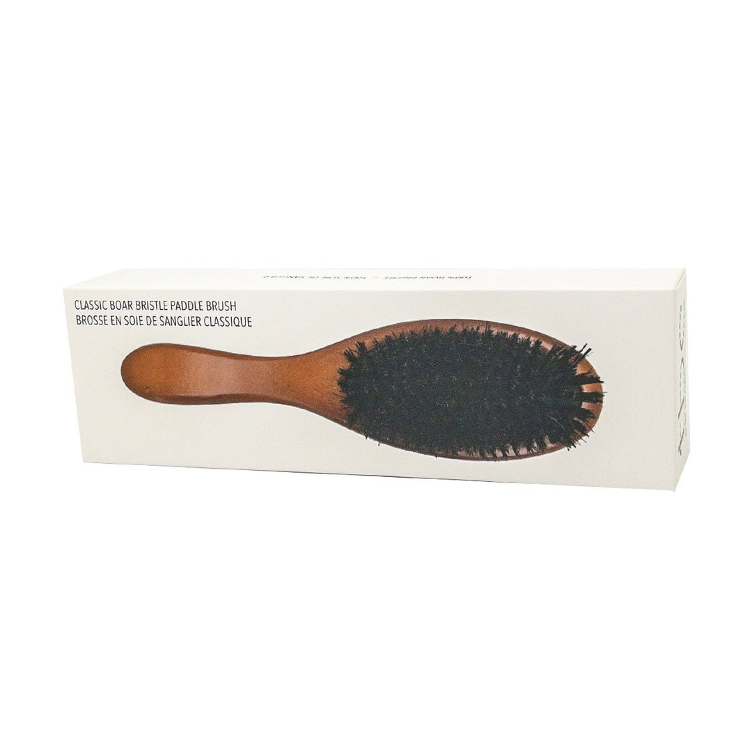 En rektangulær æske viser TBC's Classic Hårbørste med Boar Bristle paddle brush, der har et brunt træskaft og mørke børster på en almindelig hvid baggrund.