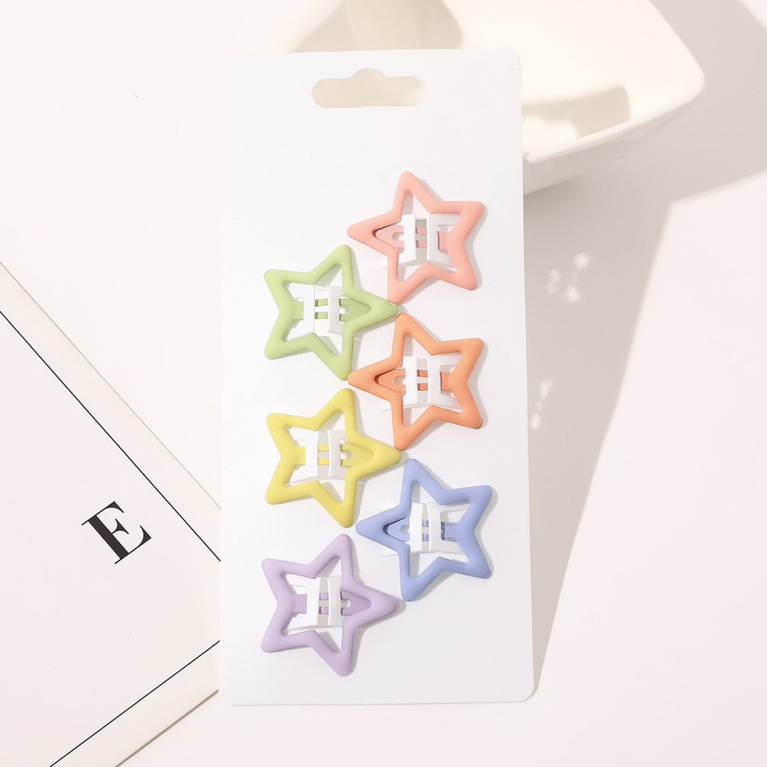 Et hvidt kort viser seks pastelfarvede SOHO Holli Hårspænder - Mat Mix hårspænder i grøn, pink, orange, gul, lilla og blå. Kortet er perfekt til børn og ligger på en hvid flade ved siden af et papir med bogstavet E.