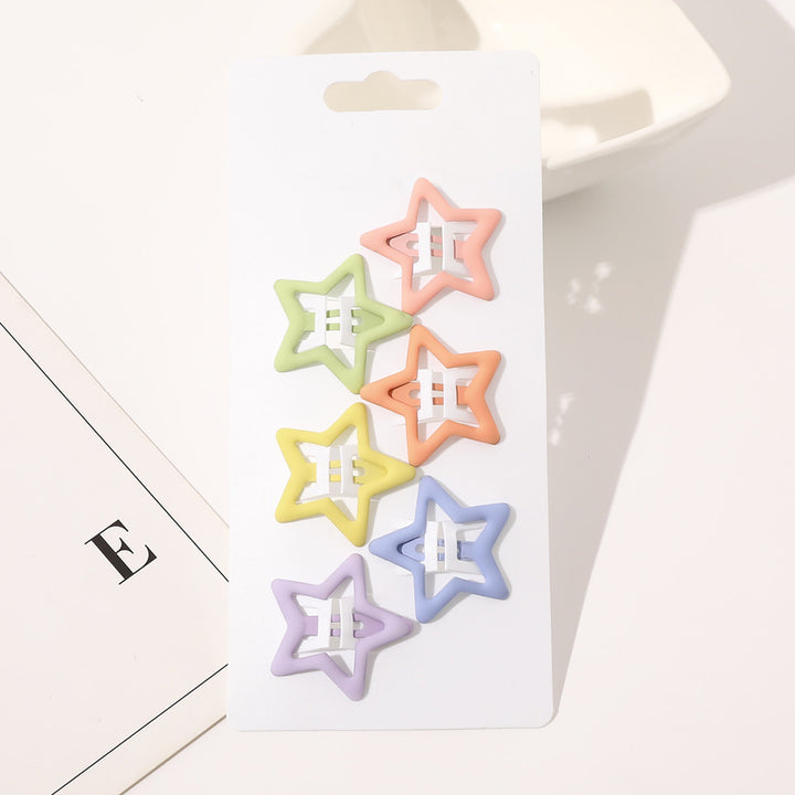 Et hvidt kort viser seks pastelfarvede SOHO Holli Hårspænder - Mat Mix hårspænder i grøn, pink, orange, gul, lilla og blå. Kortet er perfekt til børn og ligger på en hvid flade ved siden af et papir med bogstavet E.