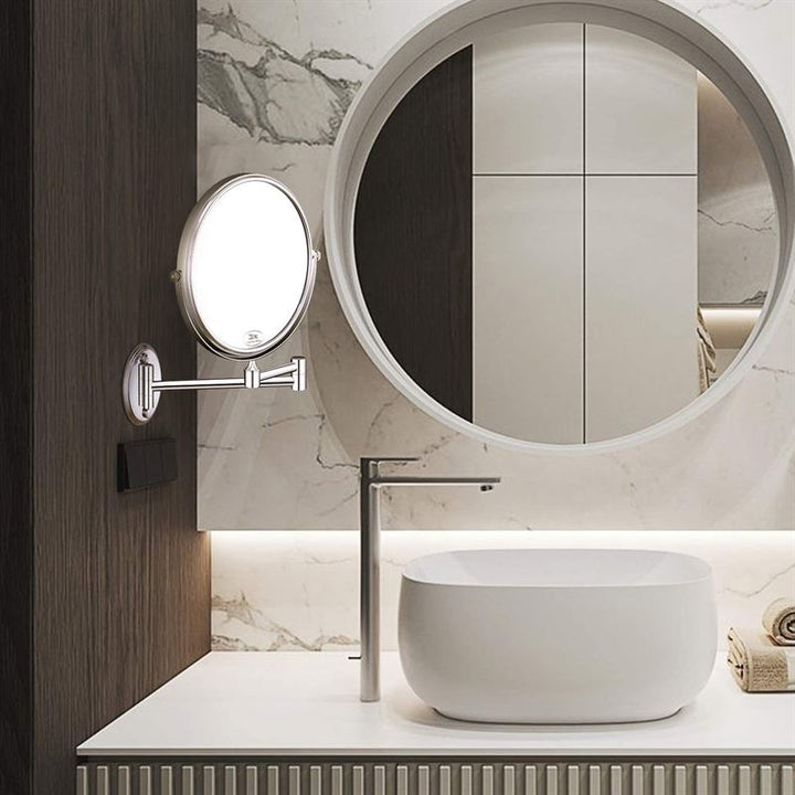 UNIQ Badeværelsesspejl med arm og forstørrelse fra UNIQ, rund form og vægmonteret lys. Rektangulær hvid vask på rillet skab, høj vandhane og håndklæder set i spejlets refleksion.