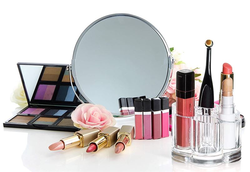 UNIQ Blomster Makeup Akryl Organizer | U301 fra UNIQ viser læbestifter, lipgloss, øjenskyggepaletter og et rundt spejl på en hvid overflade, der er dekoreret med lyserøde kunstige roser for et elegant touch.