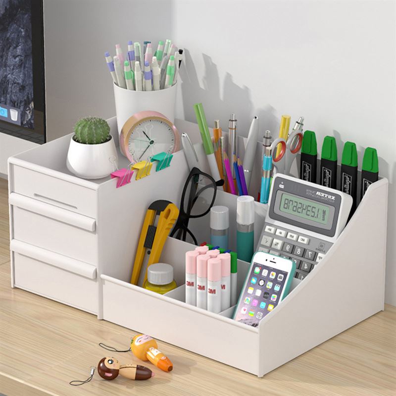 En hvid UNIQ Kosmetik Organizer | P110 fra UNIQ rummer kuglepenne, tuscher, blyanter, sakse, lommeregner, sticky notes, overstregningstuscher, en smartphone og en lille kaktus i potte - alt sammen pænt arrangeret på et skrivebord af træ.