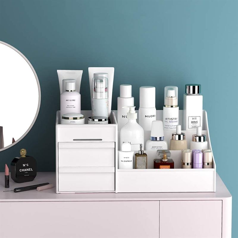 En UNIQ Kosmetik Organizer | P110 | Hvid fra UNIQ holder hudpleje- og kosmetikflasker, krukker og tuber på et toiletbord ved siden af et rundt spejl. Makeup-artikler og en sort Chanel-parfumeflaske står ved siden af mod en blå væg.