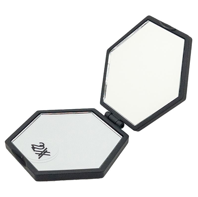 UNIQ Mini Kompakt Hexagon Spejl er et sort, sekskantet kompaktspejl med to spejle indeni - det ene med UNIQ-logoet. Perfekt som et mini makeupspejl med forstørrelse til din håndtaske, vist mod en hvid baggrund.