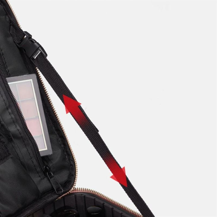 Et nærbillede af den åbne pink UNIQ Rejsetoilettaske/Kosmetiktaske til alt dit Makeup by UNIQ, der viser stroppen fremhævet med røde pile, organiseret makeupopbevaring i åbninger og en klar lomme med en makeup-palet.