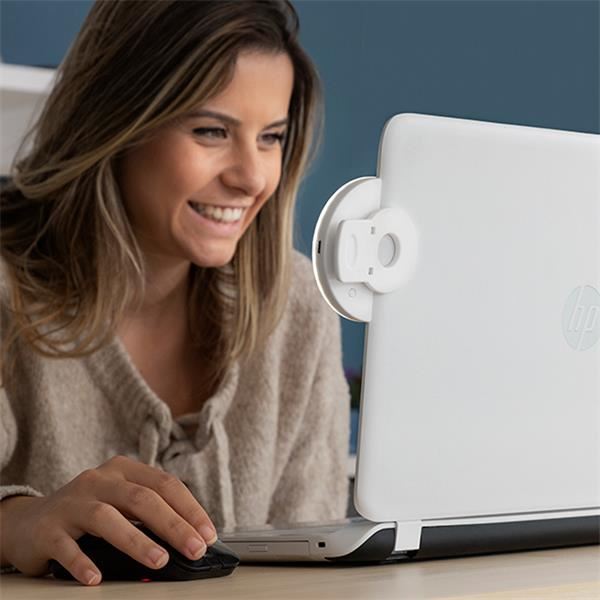 En smilende kvinde bruger en computermus foran en HP-laptop med et hvidt webcam-cover, oplyst af UNIQ Selfie LED Ringlight til Smartphones | Genopladelig fra UNIQ, der giver hende den perfekte glød til enhver selfie.