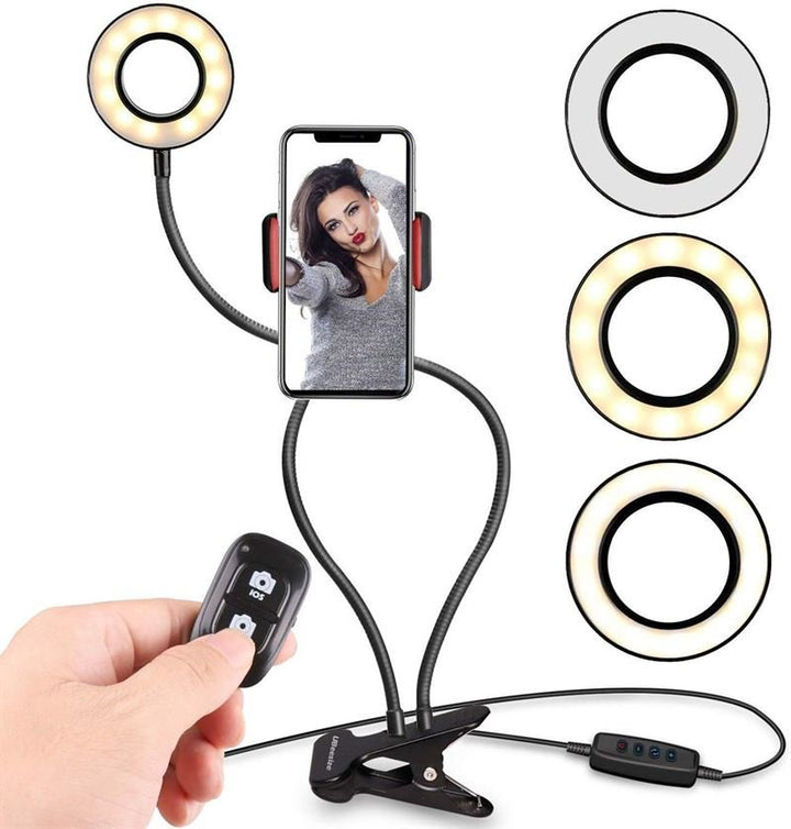 UNIQ Selfie Ringlight med LED Lys og Fleksible Arme fra UNIQ har tre LED-lys-farger, justerbare arme, fjernkontrol, telefonholder (viser en kvinde som poserer) og klemmefeste for enkel montering på overflater.