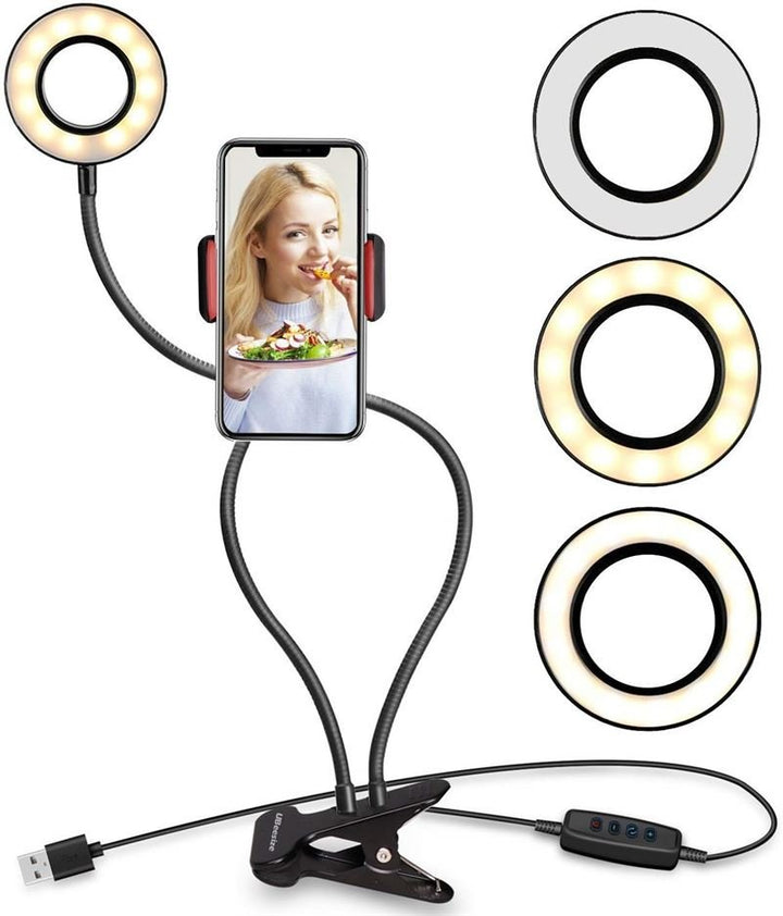 UNIQ Selfie Ringlight med LED Lys og Fleksible Arme fra UNIQ har USB-stik, klipsbase, kontrolknapper og tre LED-lysindstillinger. En smartphone i holderen viser en kvinde spise under professionelt lys.