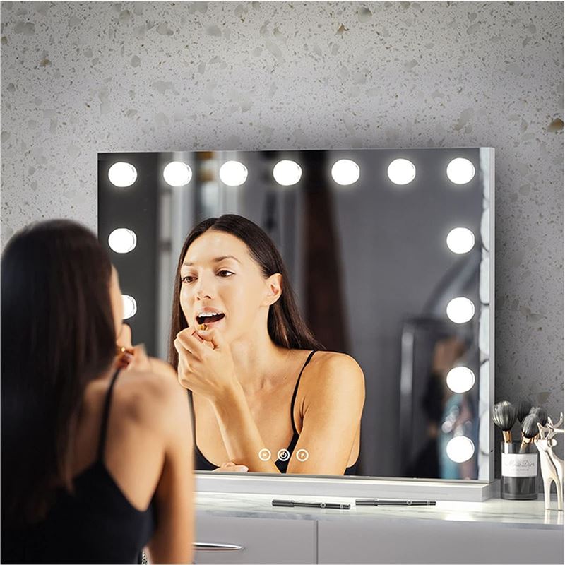 En kvinde lægger læbestift foran en UNIQ XL Hollywood Makeup Spejl med lys fra UNIQ, udstyret med 15 LED pærer og touch funktion, mens makeupbørster og -værktøjer ligger på bordet foran hende.