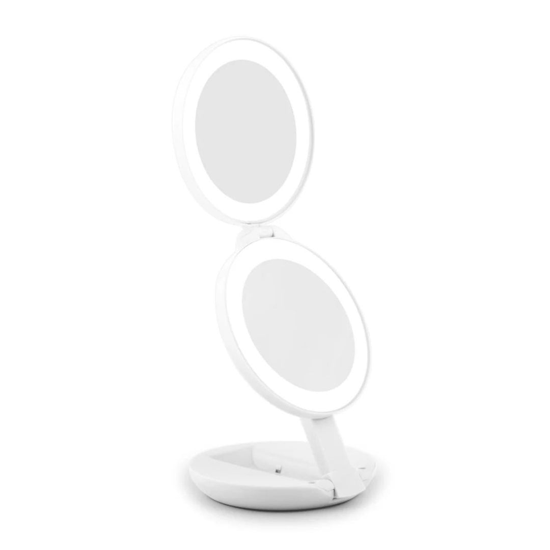 UNIQ Kompakt dobbelt rejsespejl med LED (10x forstørrelse) i hvid er et rundt, dobbeltsidet makeupspejl med indbygget LED-belysning, her vist i åben tilstand på sin cirkulære fod foran en ensfarvet hvid baggrund.