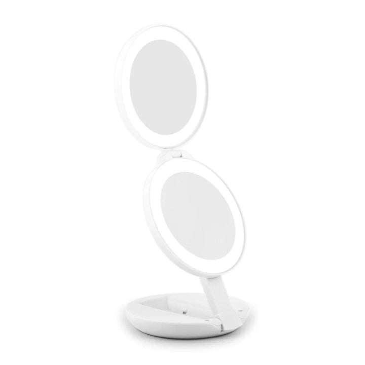 UNIQ Kompakt dobbelt rejsespejl med LED (10x forstørrelse) i hvid er et rundt, dobbeltsidet makeupspejl med indbygget LED-belysning, her vist i åben tilstand på sin cirkulære fod foran en ensfarvet hvid baggrund.