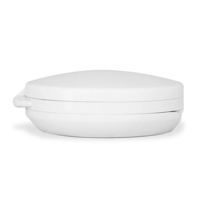 Et billede set fra siden af UNIQ Kompakt dobbelt rejsespejl med LED (10x forstørrelse) – Hvid, et lukket, rundt, hvidt rejsespejl i plast fra UNIQ med et elegant, minimalistisk design og diskret LED-belysning, vises på en ensfarvet hvid baggrund.