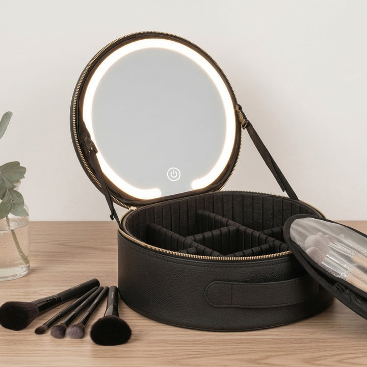 UNIQ Sort LED-makeupspejl med 3-farvet lys og praktisk opbevaring – Rejse-makeup-tasken fra UNIQ er en rund, sort makeup-taske med et åbent låg, der har et oplyst LED-makeup-spejl og opdelte indvendige rum til smart opbevaring. Den er omgivet af makeup-børster på bordet og en lille glasvase med grønne blade ved siden af.