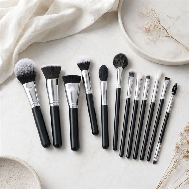 Et Technique PRO Galactic Ray-makeupbørstesæt, der består af tolv makeupbørster med sorte skafter, herunder både øjenbørster og ansigtsbørster i forskellige former og størrelser, er pænt anbragt på en lys overflade med plader i neutrale farver og tørrede planter i baggrunden.
