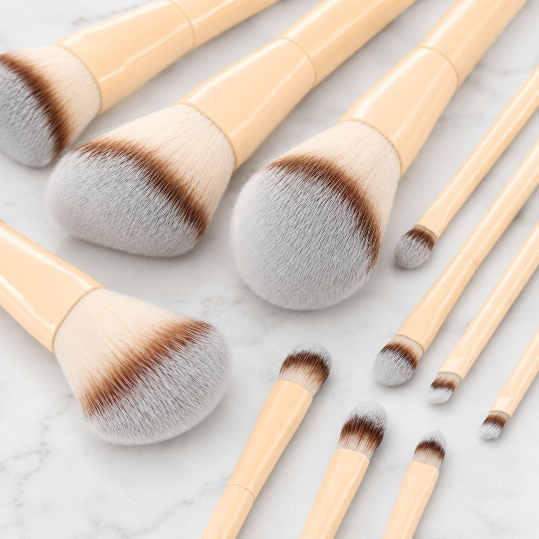 Et sæt Technique PRO Buttercream Makeupbørste Sæt – bestående af 10 makeupbørster med beige skafter og bløde, fyldige børstehår – er elegant anbragt på en hvid marmoroverflade – perfekt til at skabe et fejlfrit look med dine yndlingsfoundationbørster.