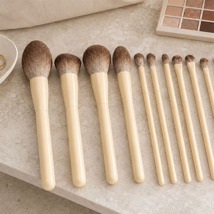 Technique PRO Vanilla Makeupbørste Sæt indeholder fjorten makeupbørster med beige skafter i forskellige størrelser, som alle er pænt anbragt på en beige overflade ved siden af en øjenskyggepalet – hvilket gør det til det perfekte supplement til din makeuprutine.