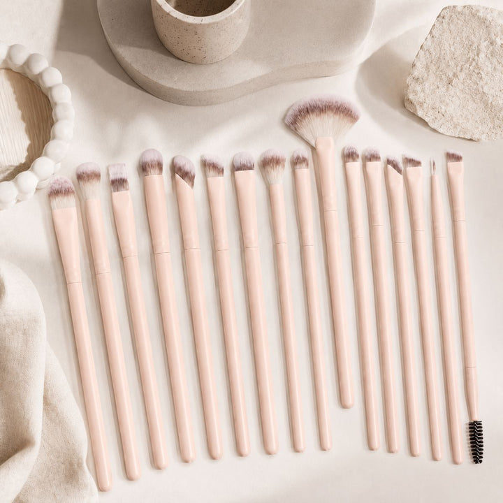 Et sæt bestående af seksten Technique PRO Keen Eyeshadow, Eyebrow & Detailing-makeupbørster med lyserøde skafter i forskellige former og størrelser, der er perfekte til påføring af øjenmakeup, pænt anbragt på en lys, struktureret overflade med dekorative genstande i nærheden.