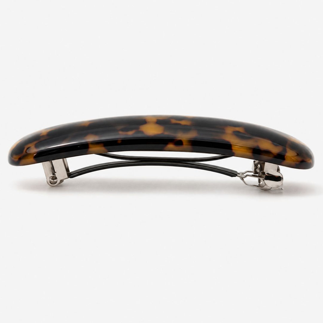 SOHO Mila Barrette Hårspænde – Dark Tortoise fra SOHO har en buet plasttop i et klassisk skildpaddemønster og en robust metalklips med kliklås, præsenteret på en ensfarvet hvid baggrund.