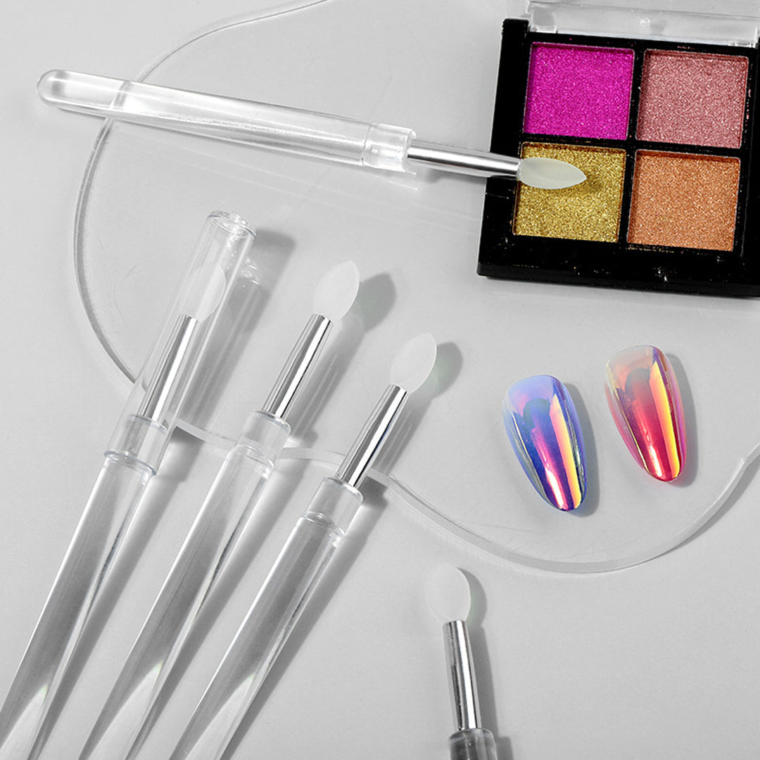 Universel Makeup Dubbe-børste i silikone fra Technique PRO til præcis påføring på læber, negle og øjenskygge, præsenteret sammen med en palet med fire skinnende øjenskygger i rosa, guld- og kobbernuancer samt to iriserende kunstige negle – alt sammen udstillet på en hvid overflade.
