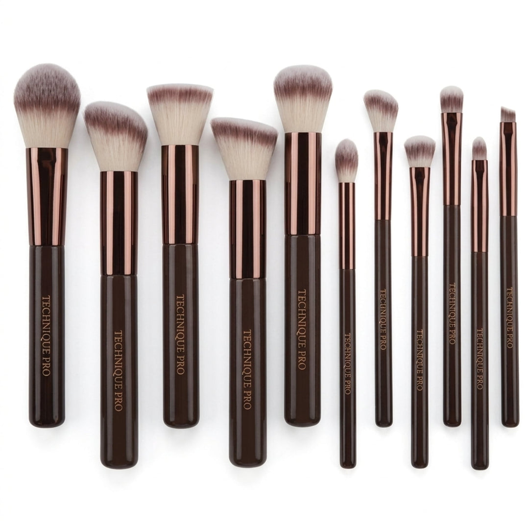 Et sæt bestående af elleve Technique PRO Chocolate Bronze Makeupbørste Sæt – 11 makeupbørster med brune skafter og metalliske hylster, anbragt på række.