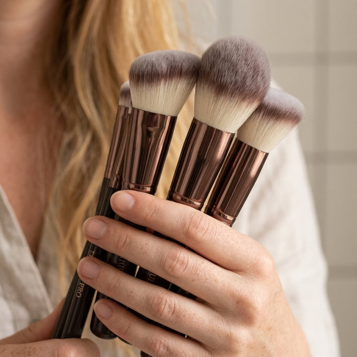 En hånd holder et sæt Technique PRO Chocolate Bronze Makeupbørste Sæt med mørke skafter, metalliske rør og bløde, tofarvede børstehår.