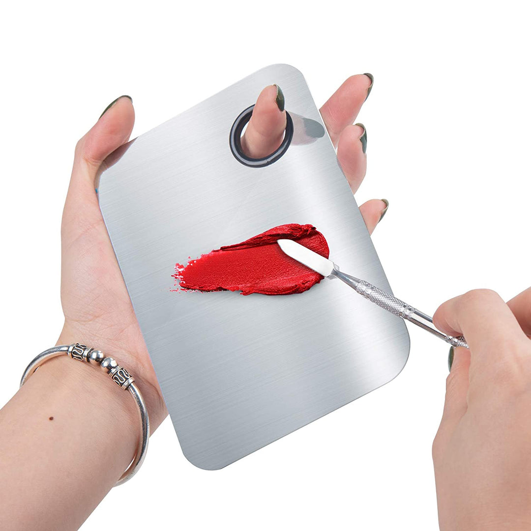 En hånd holder »Technique PRO Professional Makeup Mixing Palette« og blander på mesterlig vis rød læbestift med en spatel, mens den anden hånd holder paletten fast.