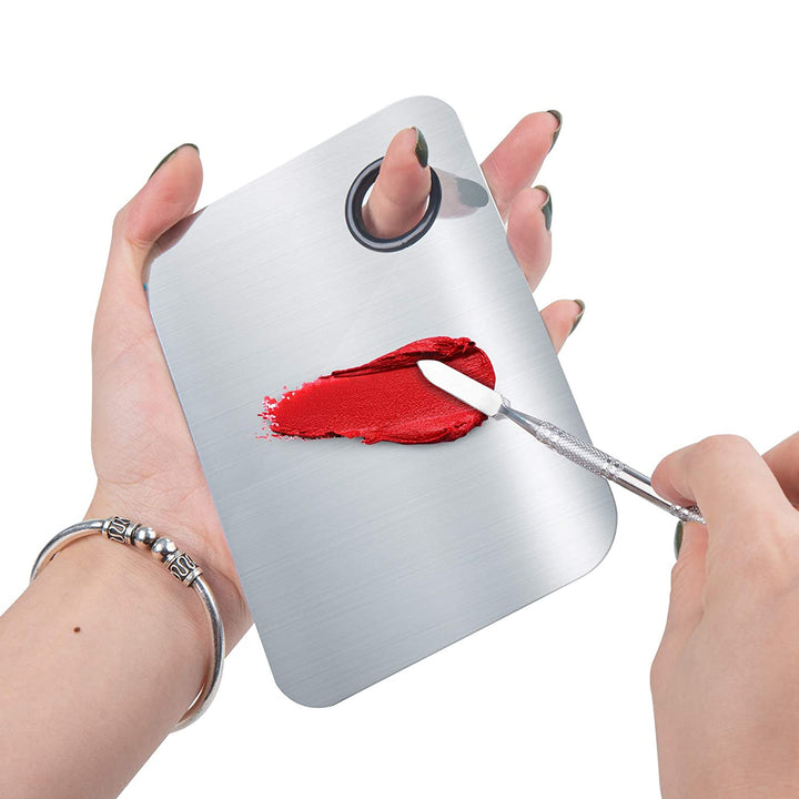 En hånd holder »Technique PRO Professional Makeup Mixing Palette« og blander på mesterlig vis rød læbestift med en spatel, mens den anden hånd holder paletten fast.