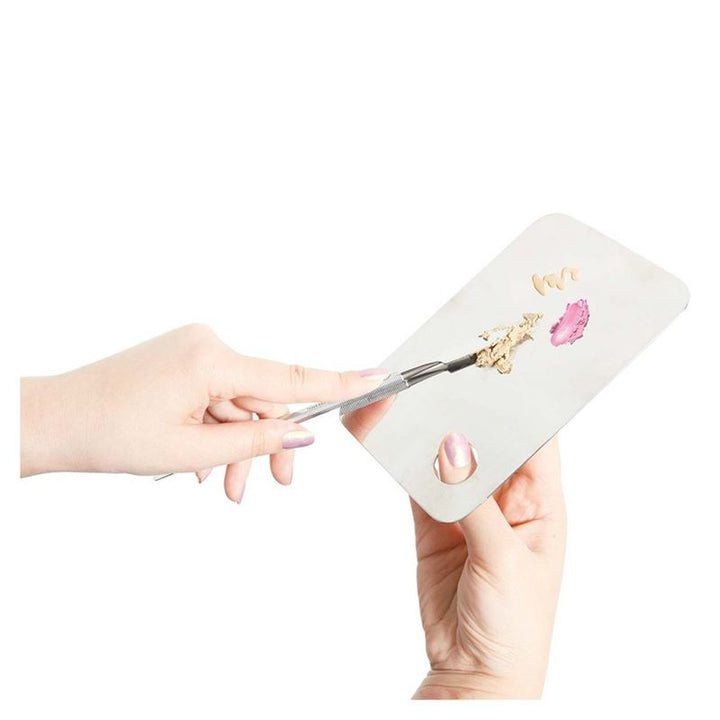 To hænder holder Technique PRO Professional Makeup Mixing Palette og en spatel. Forskellige nuancer af foundation og lyserød creme-makeup blandes mesterligt på paletten, hvilket viser præcise teknikker til at blande foundation.