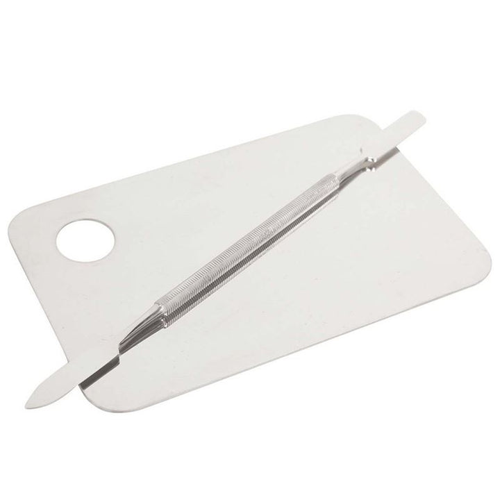 En »Technique PRO Professional Makeup Mixing Palette« af rustfrit stål står med en metalspatel placeret diagonalt hen over den rektangulære overflade, der har et rundt hul i det ene hjørne – begge dele er ideelle til at udjævne foundation eller blande kosmetik og maling.