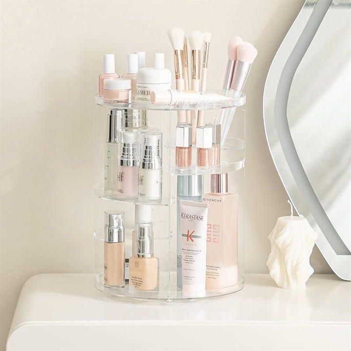 UNIQ 360 graders roterende organizer - Transparent fra UNIQ har plads til hudplejeflasker, makeupbørster, lotion og skønhedsprodukter på en beige bordplade ved siden af et dekorativt lys og et spejl.