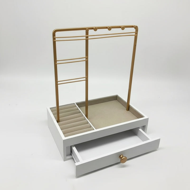 UNIQ smykkestativ / smykkeskrin i guld med skuffe – Holder til øreringe, ringe og kæder (29 cm) fra UNIQ er en elegant hvid smykkeopbevarer med et guldfarvet stativ til ophængning af smykker, polstrede ringholdere, en åben bakke og en åben skuffe med et lille rundt guldhåndtag – perfekt til stilfuld smykkeopbevaring. Fotograferet på en ensfarvet hvid baggrund.
