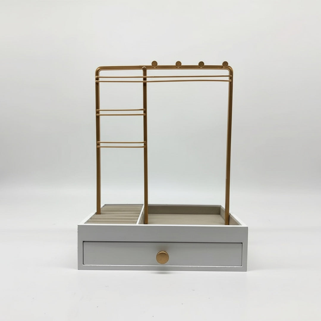 UNIQ Smykkestativ / Smykkeskrin i Guld med Skuffe er en stilfuld hvid smykkeopbevaring fra UNIQ. Den består af et elegant smykkestativ i guldmetal til ophængning af øreringe, ringe og halskæder samt en lille bakke og en skuffe i bunden prydet med en rund guldknap – alt sammen på en enkel hvid baggrund.